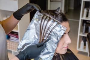Closeup of hairdresser hands separating strands of hair of beautiful young woman with aluminium foil before change the hair color